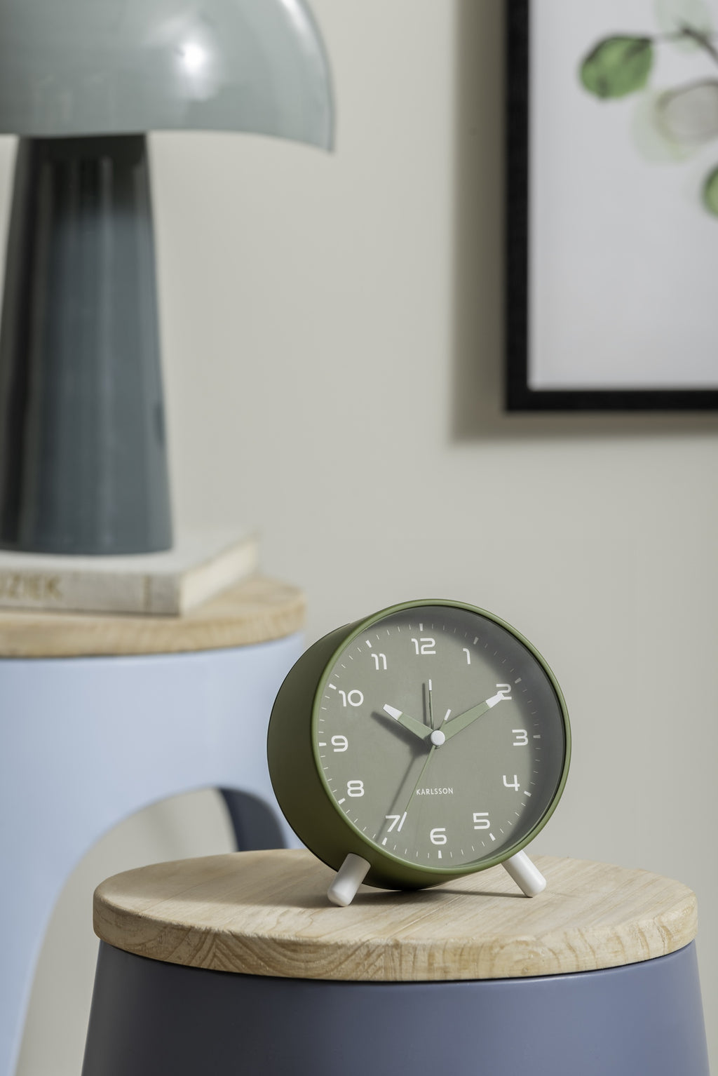 Karlsson wekker Orgullo, legergroen, sfeerfoto: op houten krukje naast blauwe kruk met lamp en boeken