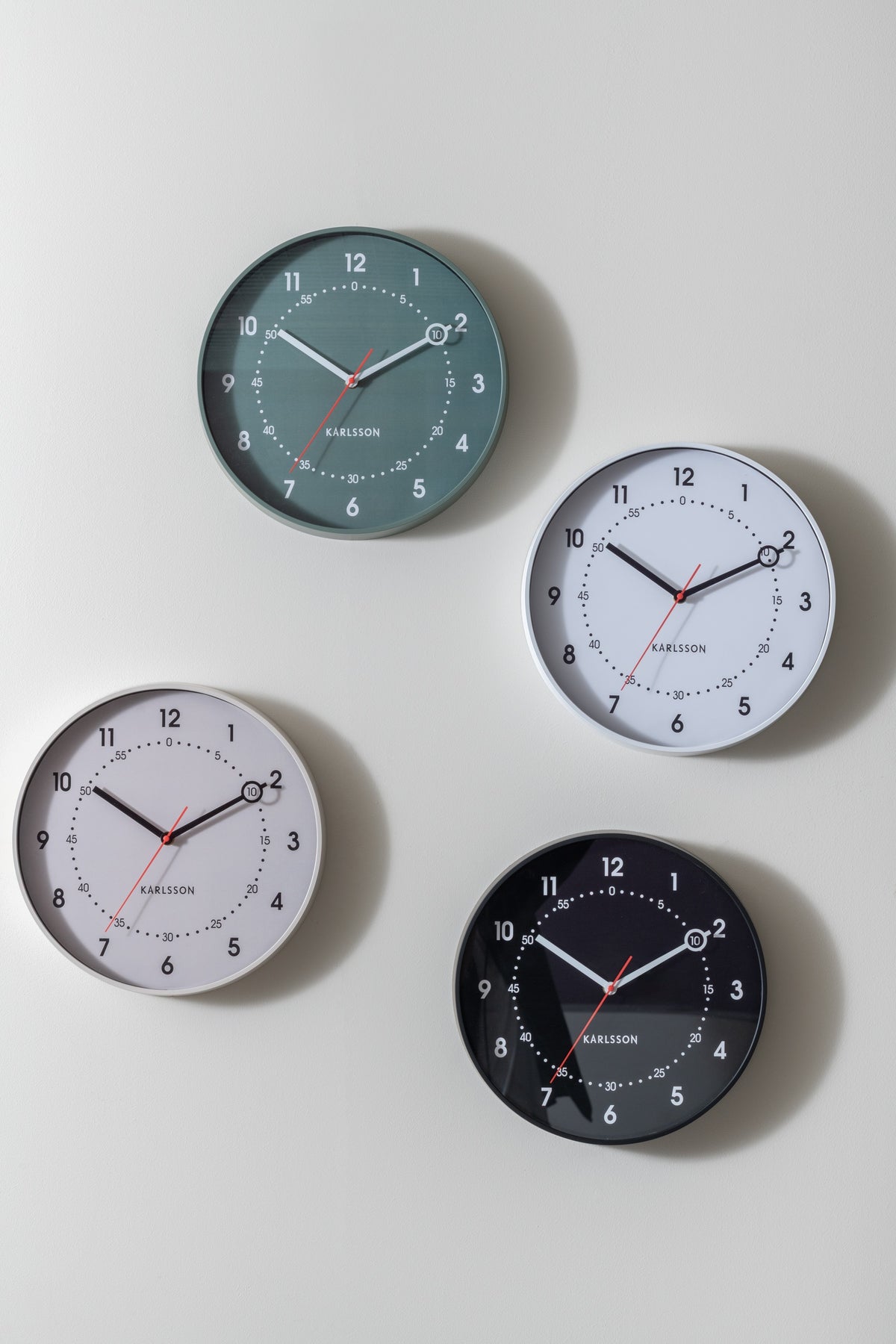 Karlsson wandklok Fresco, zwart, sfeerfoto: groepsfoto: vier kleuren (groen, wit, grijs, zwart) samen aan witte muur