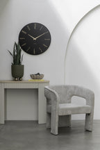 Karlsson wandklok Esmerado Large, zwart, sfeerfoto: aan witte muur boven sidetable met plant, naast grijze fauteuil