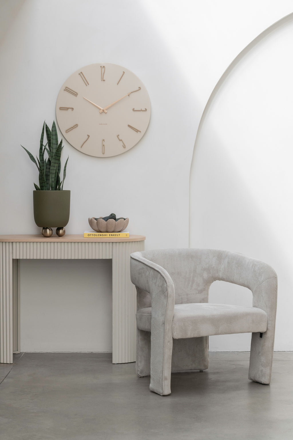 Karlsson wandklok Esmerado Large, wit, sfeerfoto: aan witte muur boven sidetable met plant, naast grijze fauteuil