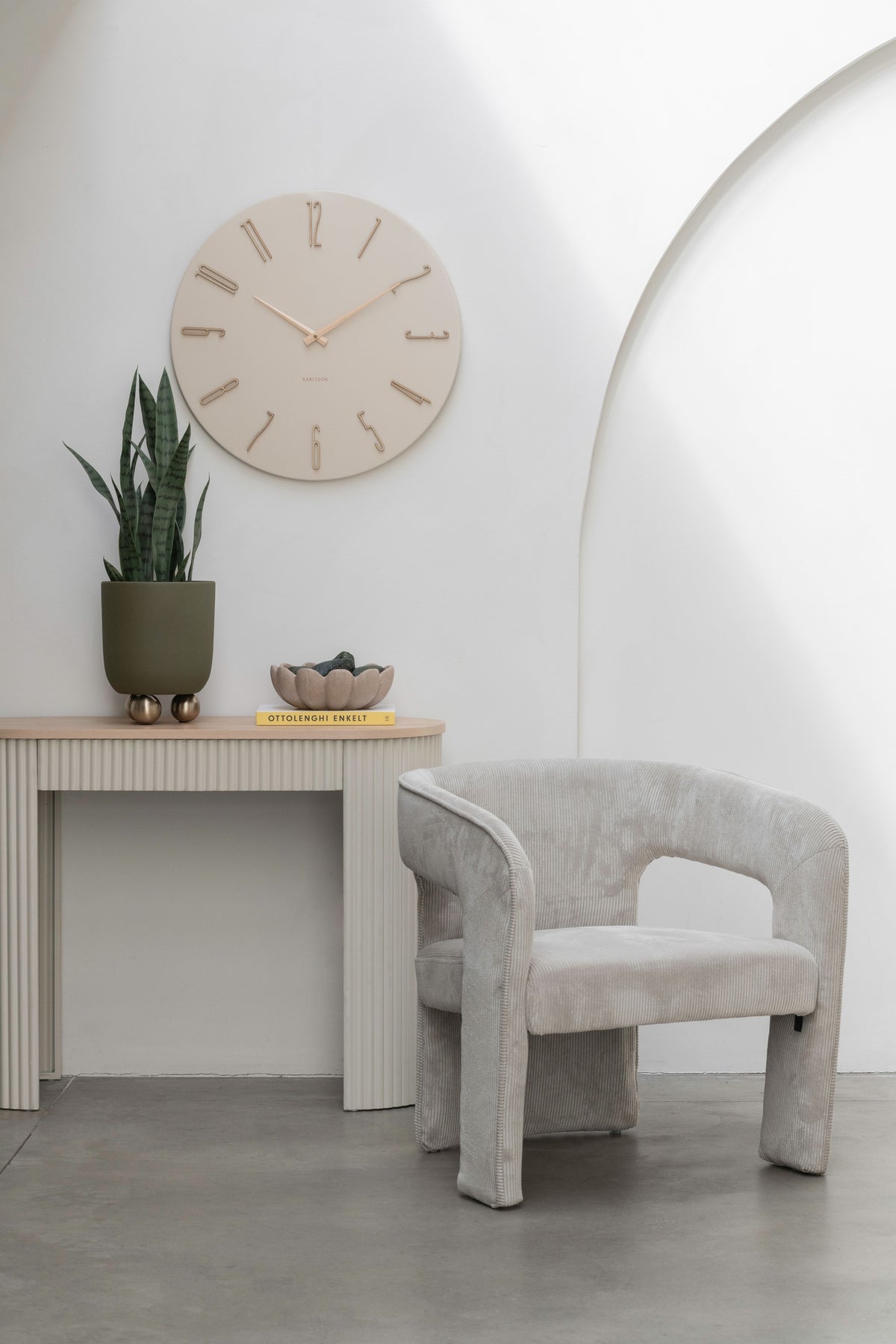 Karlsson wandklok Esmerado Large, wit, sfeerfoto: aan witte muur boven sidetable met plant, naast grijze fauteuil