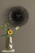 Karlsson wandklok Polo, zwart, sfeerfoto: aan taupe muur boven glazen vaas met oranje gerbera