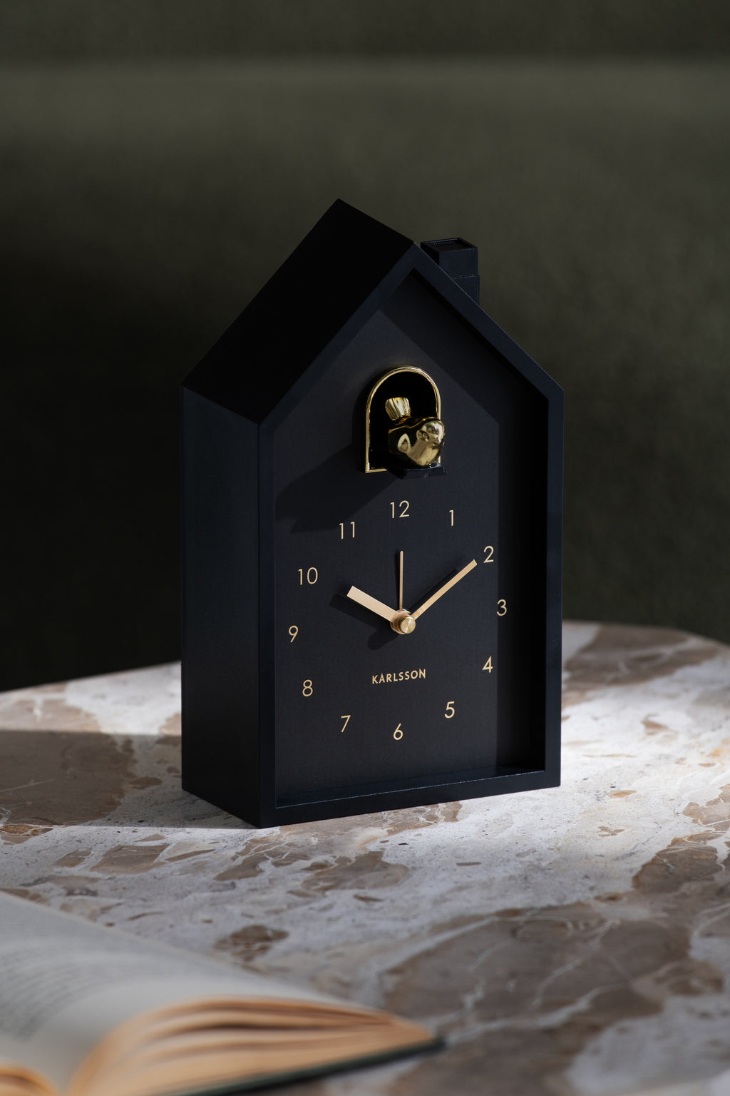 Karlsson wekker Modern Cuckoo Oro, zwart, sfeerfoto: staand op marmeren tafel naast open boek