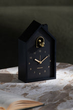 Karlsson wekker Modern Cuckoo Oro, zwart, sfeerfoto: staand op marmeren tafel naast open boek