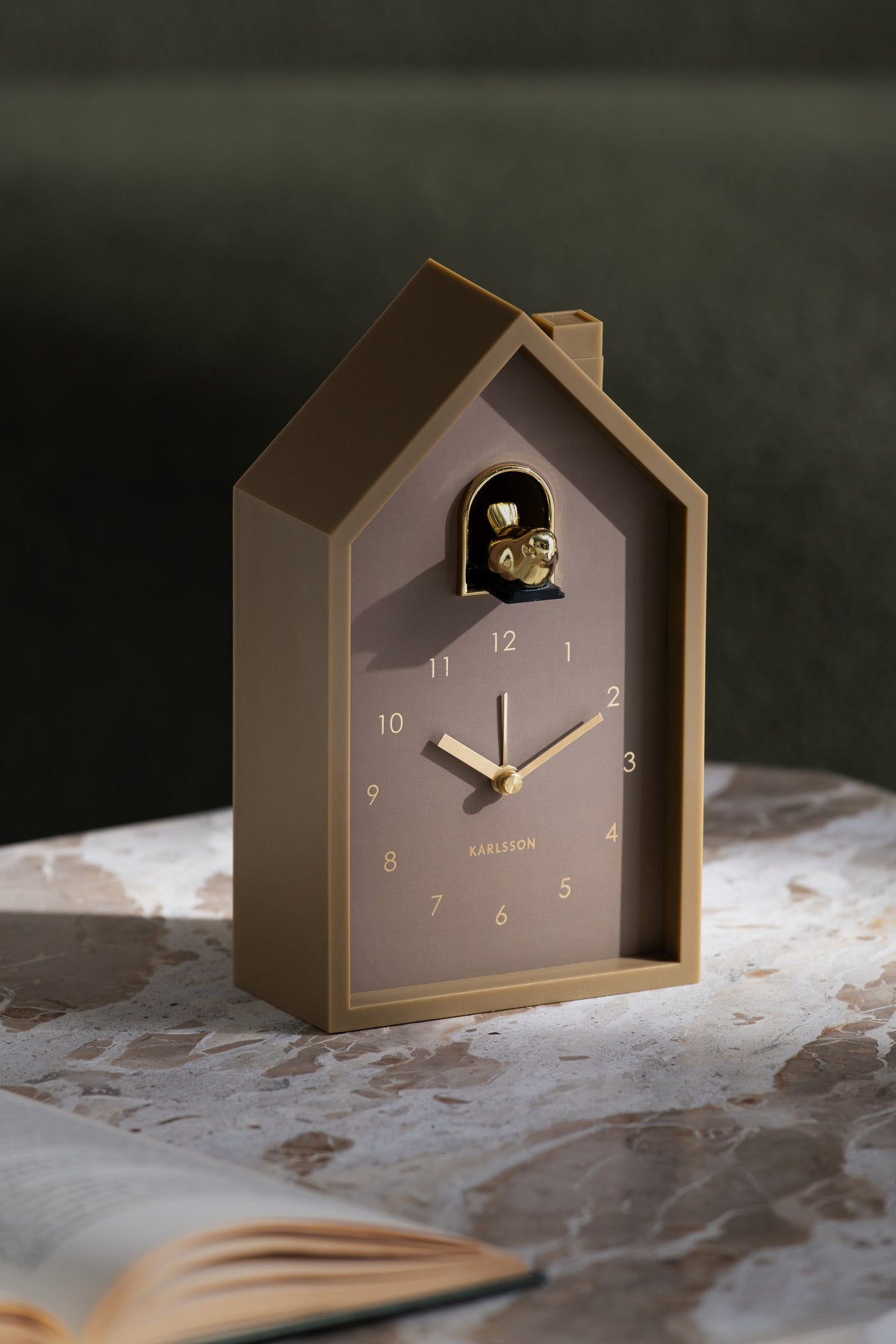 Karlsson wekker Modern Cuckoo Oro, bruin, sfeerfoto: staand op marmeren tafel naast open boek