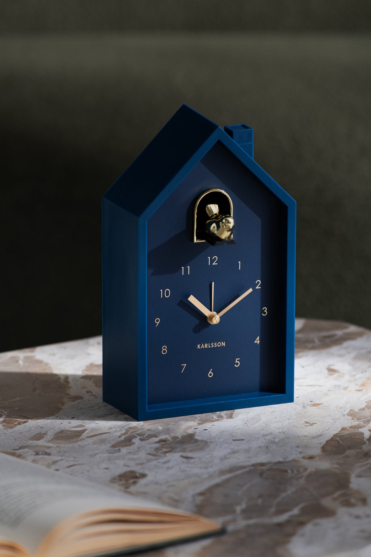 Karlsson wekker Modern Cuckoo Oro, blauw, sfeerfoto: staand op marmeren tafel naast open boek