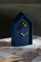 Karlsson wekker Modern Cuckoo Oro, blauw, sfeerfoto: staand op marmeren tafel naast open boek