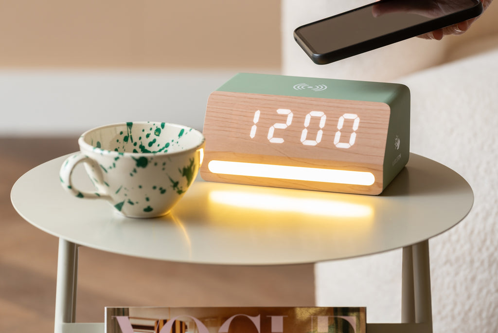 Karlsson wekker Retro LED, jungle groen, sfeerfoto: op bijzettafel met gevlekte mok, hand met telefoon boven de wekker