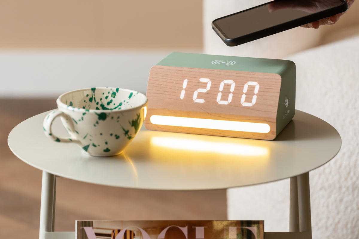 Karlsson wekker Retro LED, jungle groen, sfeerfoto: op bijzettafel met gevlekte mok, hand met telefoon boven de wekker