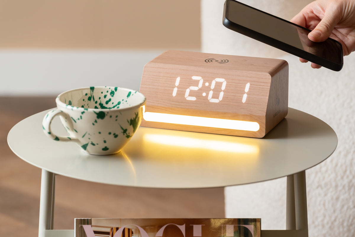 Karlsson wekker Retro LED, licht hout, sfeerfoto: op bijzettafel met gevlekte mok, hand met telefoon boven de wekker