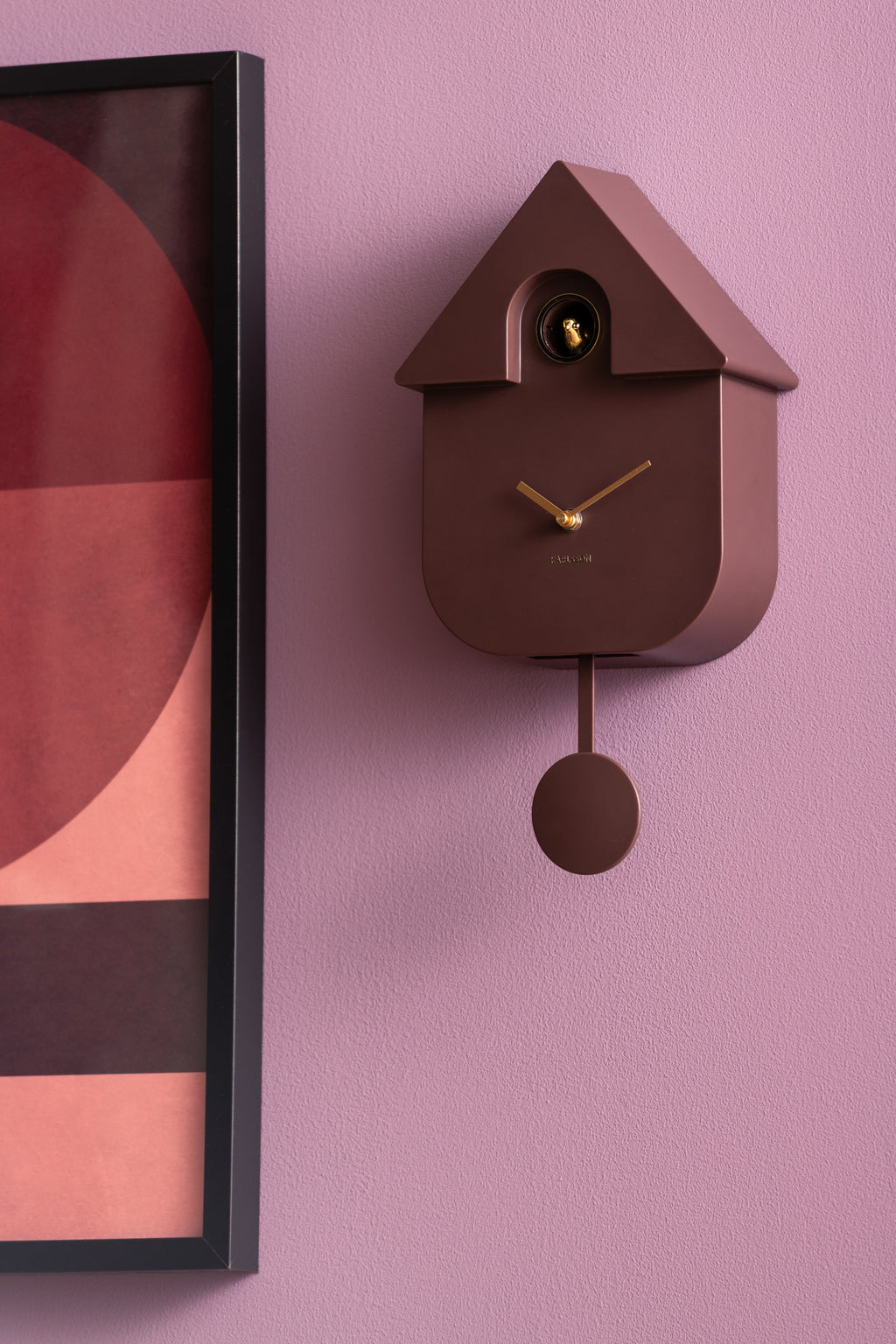 Karlsson koekoeksklok Modern Cuckoo Oro, bruin, sfeerfoto: aan lila muur naast ingelijste poster
