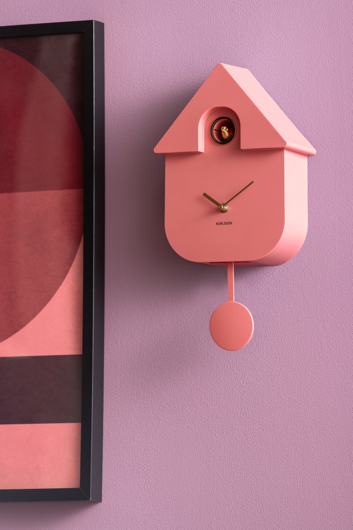 Karlsson koekoeksklok Modern Cuckoo Oro, roze, sfeerfoto: aan lila muur naast ingelijste poster