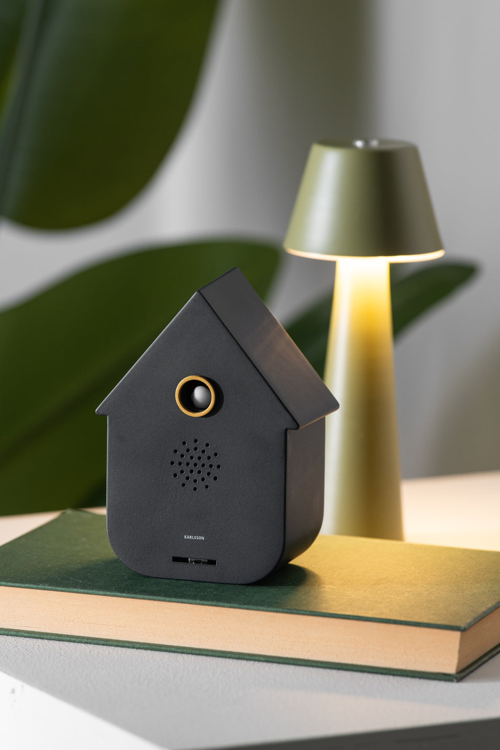 Karlsson vogelhuisje met geluid (soundbox) Modern Cuckoo, zwart, sfeerfoto: op groen boek naast groene tafellamp en plant
