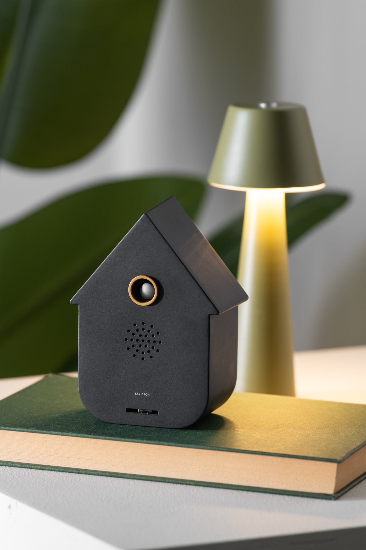 Karlsson vogelhuisje met geluid (soundbox) Modern Cuckoo, zwart, sfeerfoto: op groen boek naast groene tafellamp en plant