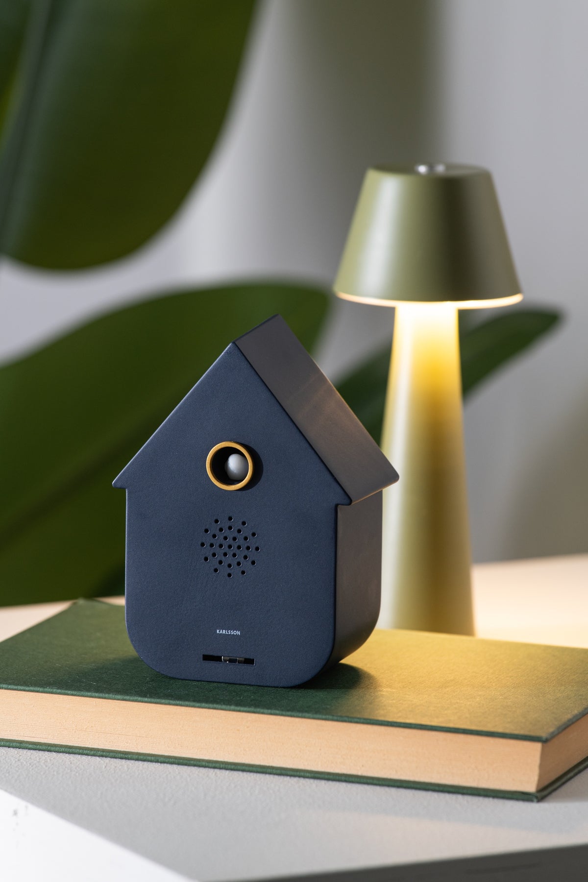 Karlsson vogelhuisje met geluid (soundbox) Modern Cuckoo, blauw, sfeerfoto: op groen boek naast tafellamp en plant