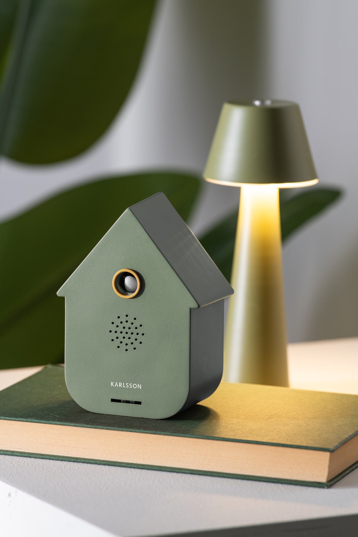Karlsson vogelhuisje met geluid (soundbox) Modern Cuckoo, groen, sfeerfoto: op groen boek naast tafellamp en plant