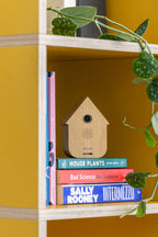 Karlsson vogelhuisje met geluid (soundbox) Modern Cuckoo, licht hout, sfeerfoto: op stapel boeken in gele boekenkast