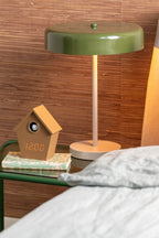 Karlsson wekker Riqueza LED, mokkabruin, sfeerfoto: op nachtkastje onder groene tafellamp naast bed, display toont 12:00
