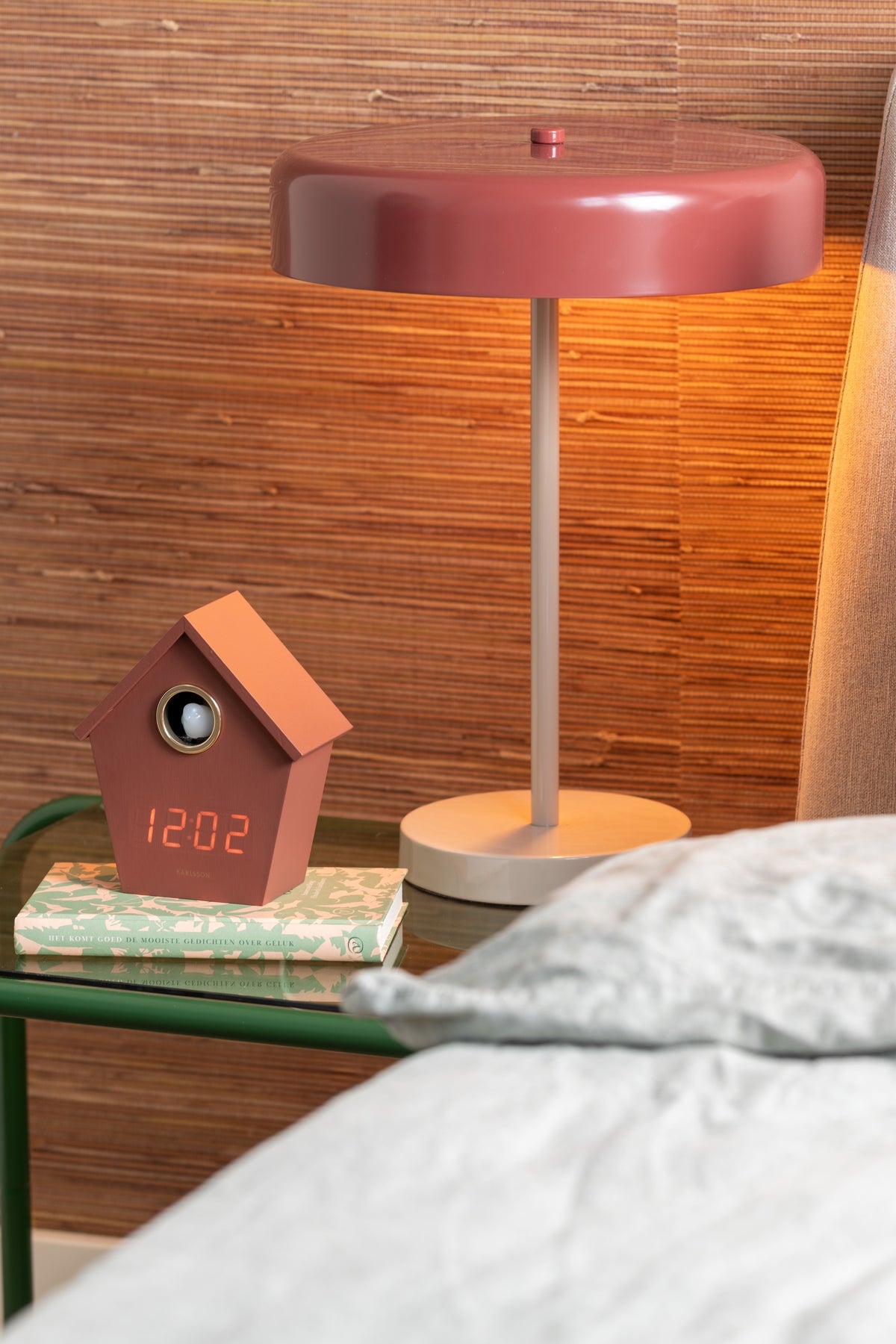 Karlsson wekker Riqueza LED, bordeauxrood, sfeerfoto: op nachtkastje op stapel boeken naast roze tafellamp en bed