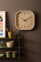 Karlsson wandklok Elemental Cuadrado, gebroken wit, sfeerfoto: aan bruine muur naast groen wandrek met servies