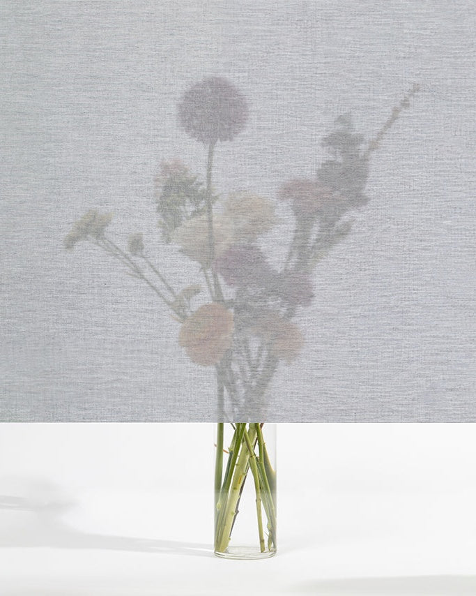 Squid raamtextiel Ash (lichtgrijs): transparant textiel voor het raam, met een boeket bloemen zichtbaar erachter