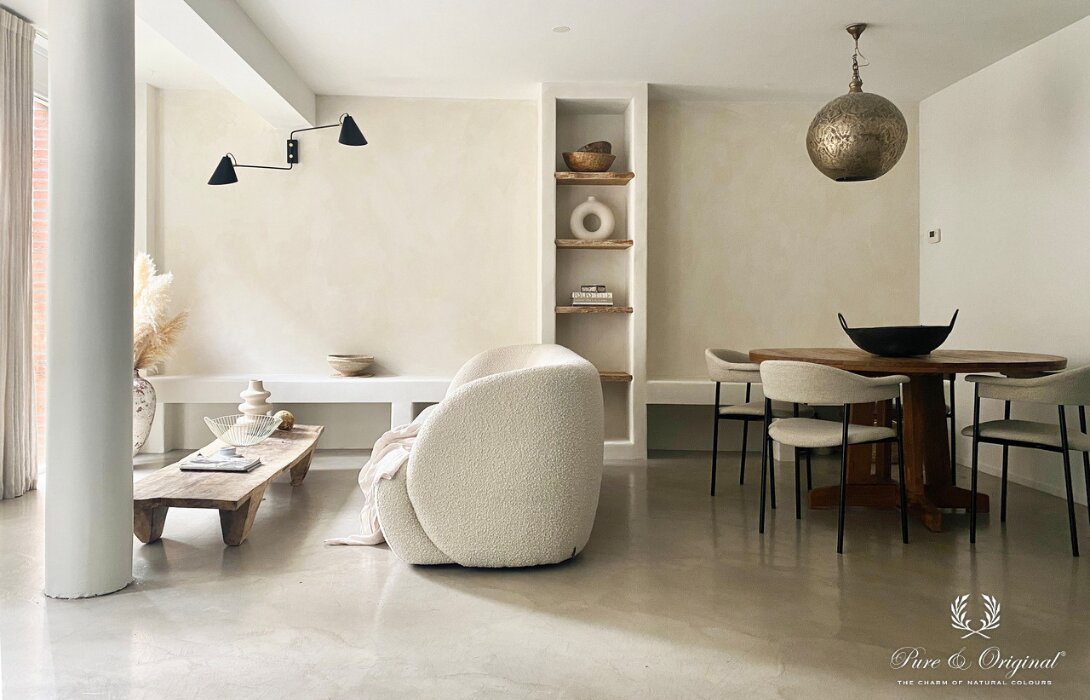 Strakke woonkamer met wanden in Pure & Original Bone, afwerking Fresco; het daglicht laat de kleur naar het raam toe lichter ogen en rechts in de schaduw donkerder.