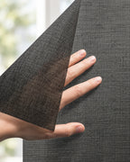 Squid raamtextiel op maat Coal - Zwart: hand tilt een hoek van het doorzichtige raamtextiel op voor een raam