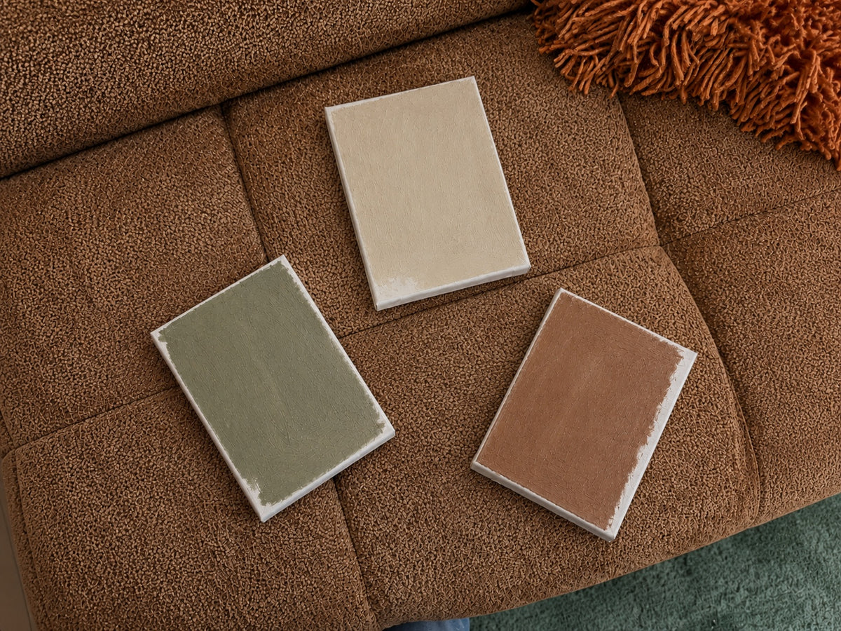 Drie verftesters op canvas in beige, groen en terracotta op een bruine bouclé bank