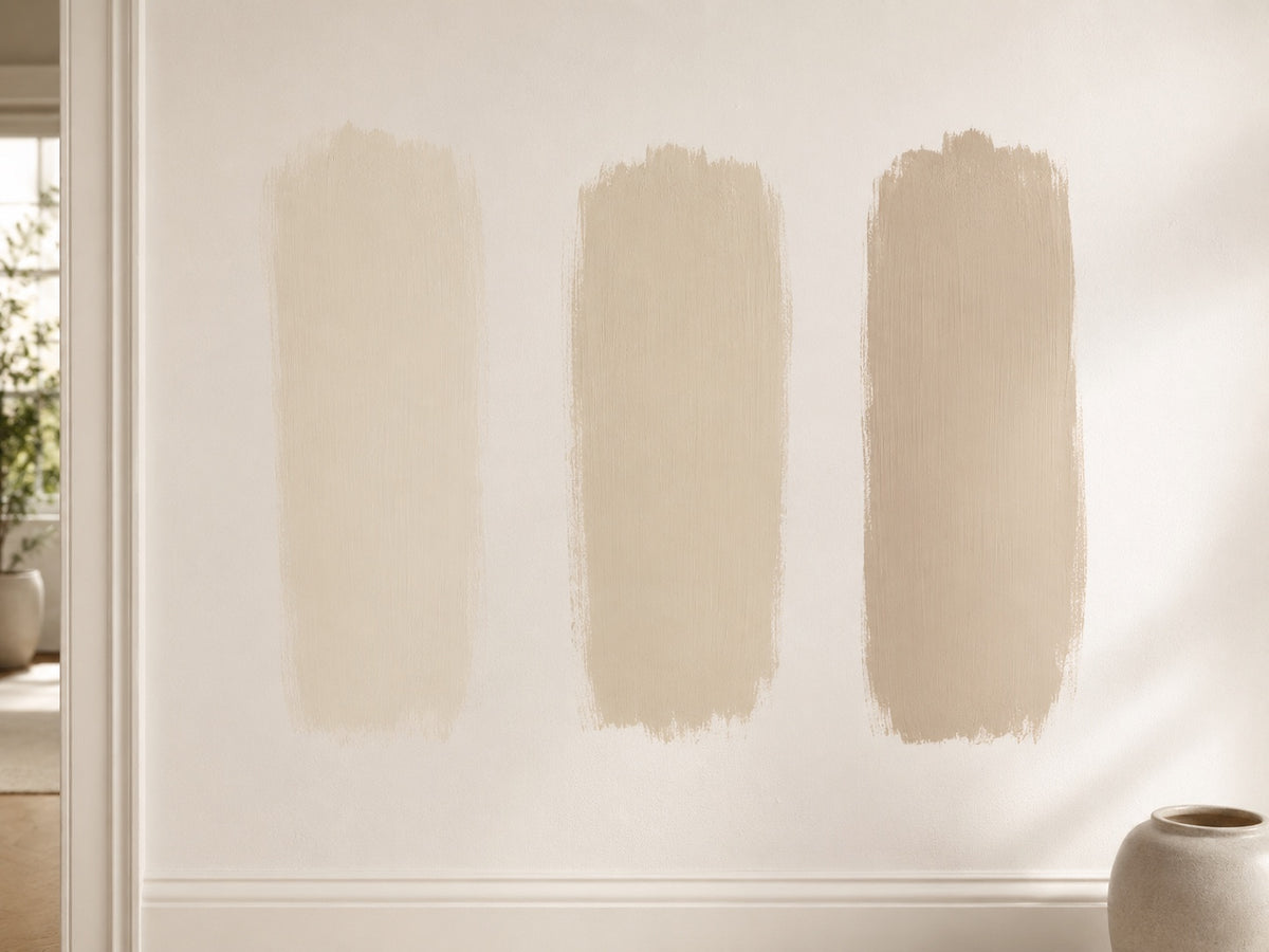 Drie beige verfstalen als penseelstreken naast elkaar op een witte muur in daglicht