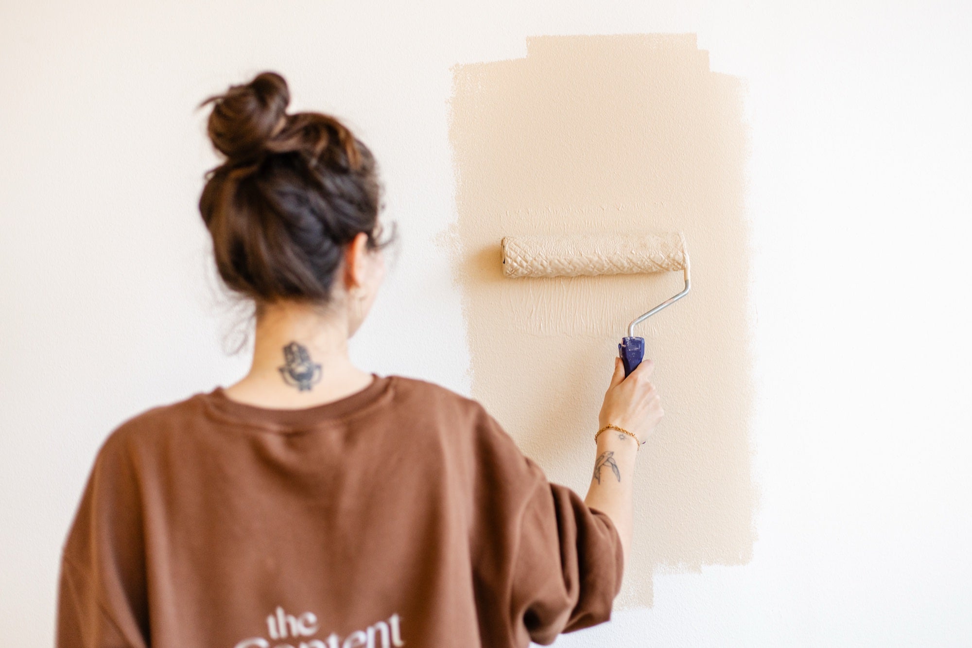 Vrouw brengt met een verfroller een beige proefvlak verf aan op een witte muur